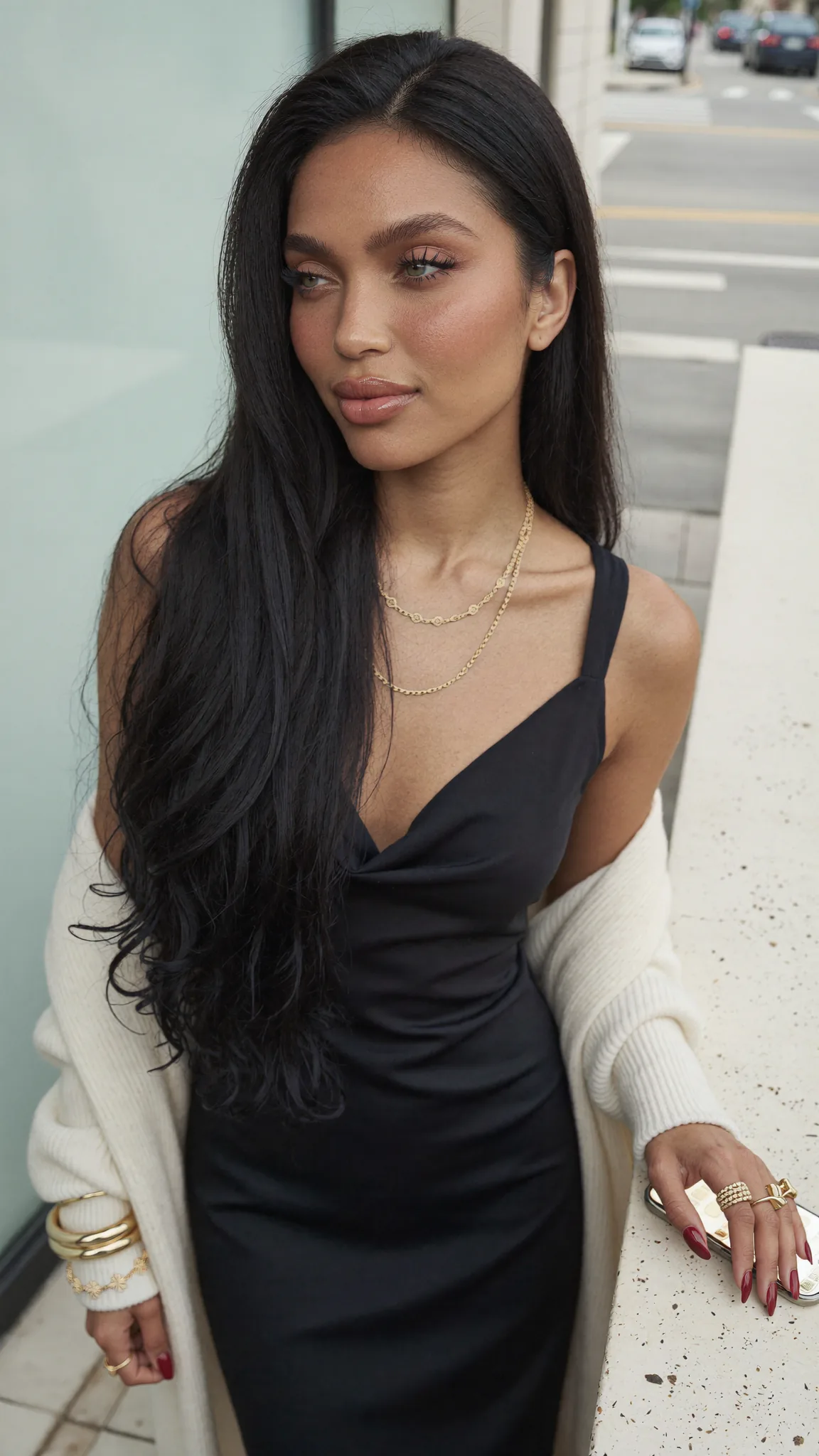 Seven Yuno in a black slip dress poses on a city sidewalk.